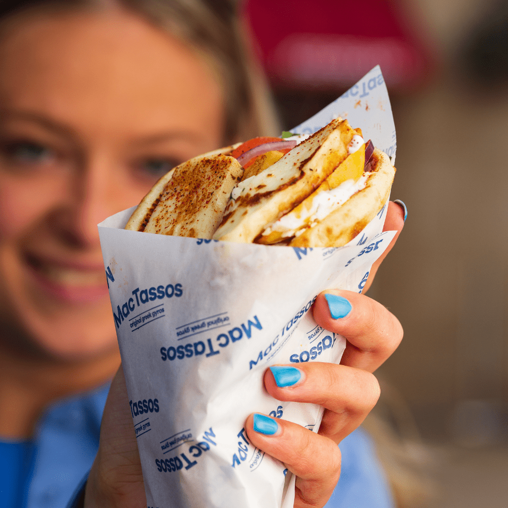 Happy MacTassos team member holding a freshly prepared Greek gyros wrap at our Glasgow street food van